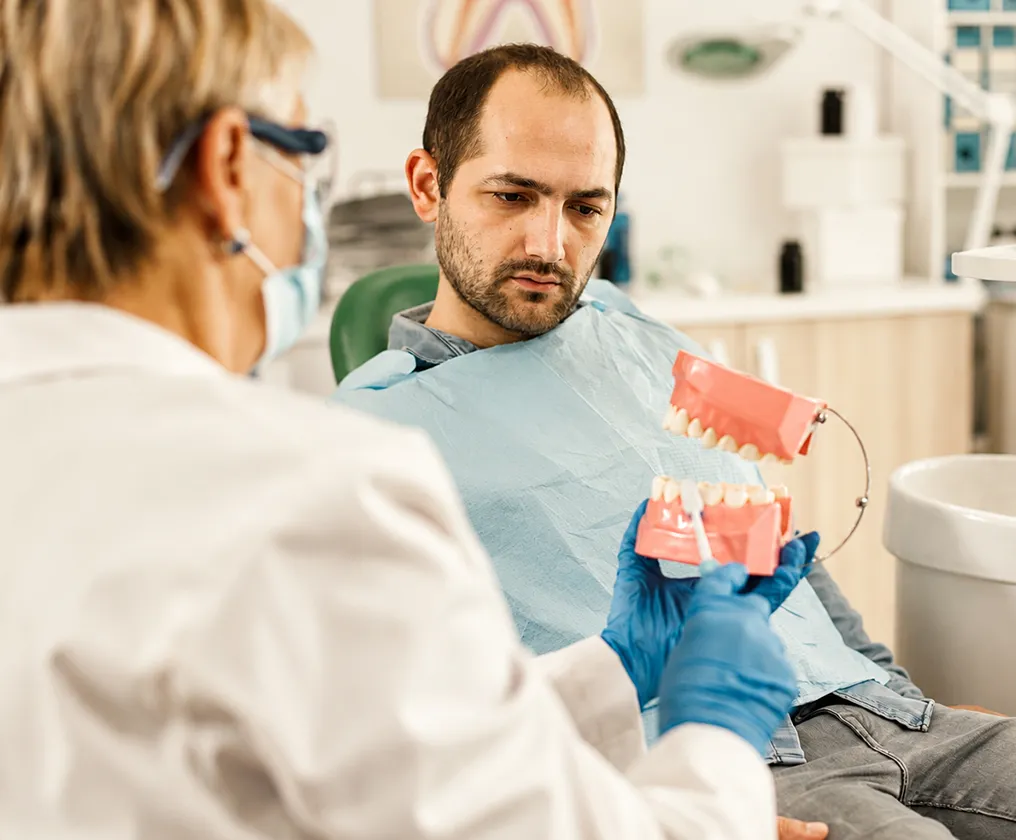 A smiling clinician demonstrating brushing on a dental model for a seated patient